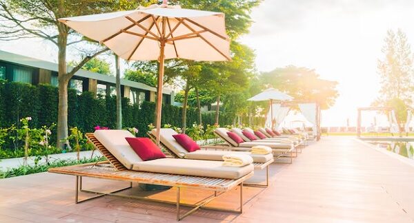 mejores resorts - una fila de tumbonas con cojines rojos y toallas blancas, ubicadas en una terraza de madera junto a una piscina en un resort. Las tumbonas están bajo sombrillas grandes y blancas