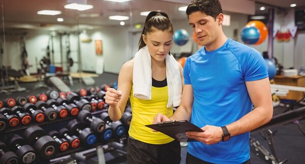 uno de los entrenadores personales, asesorando a su cliente femenina acerca del entrenamiento