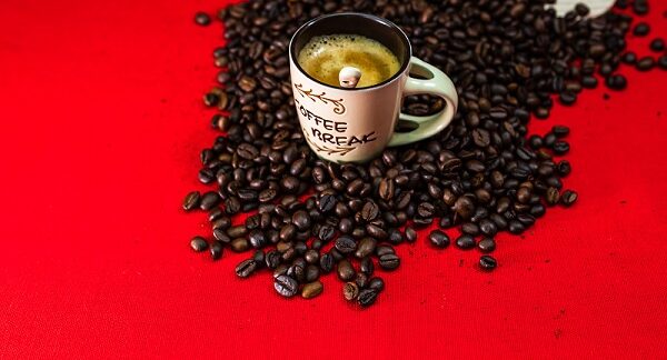 de los mejores cafés temáticos, una taza de café dispuesta encima de granos de café en un fondo rojo