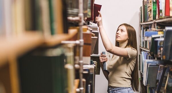 en una de las mejores librerías, una mujer selecciona un libro de un amplio librero