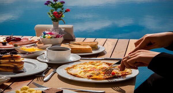 destinos populares para brunch - Mujer come tortilla con verduras, con café, panqueques, entre otros alimentos típicos para desayunar
