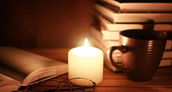 mejores libros de suspense - Una vela encendida sobre la madera, proyectando sombras inciertas sobre libros abiertos y lentes abandonados