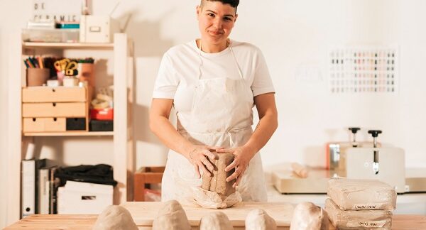 talleres de cerámica artística - una mujer sonriente con un puñado de arcilla lista para trabajar