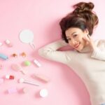 tiendas de cosméticos coreanos - mujer asiática acostada en fondo rosa junto a productos cosméticos